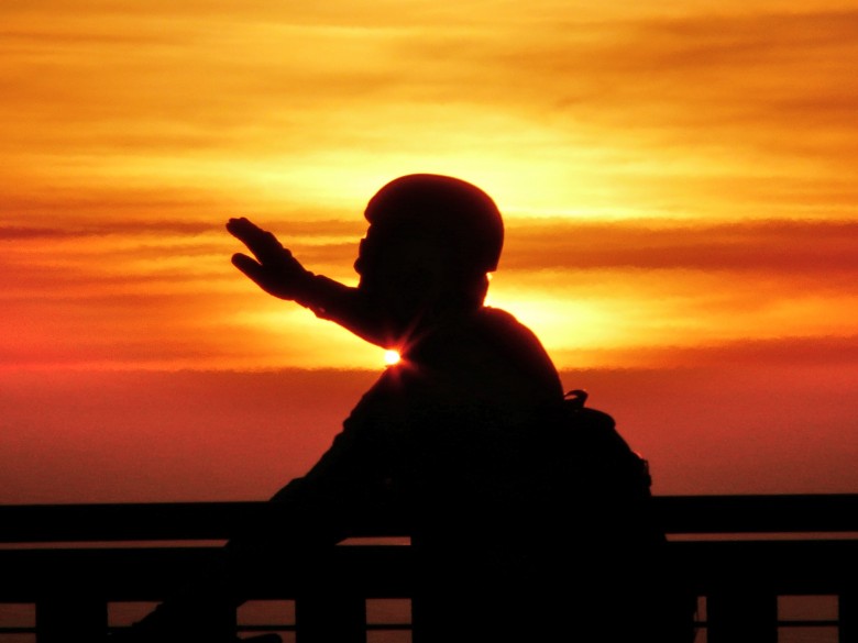 An older gentleman high 5's the sunset as he cycles across the Golden Gate Bridge in San Francisco